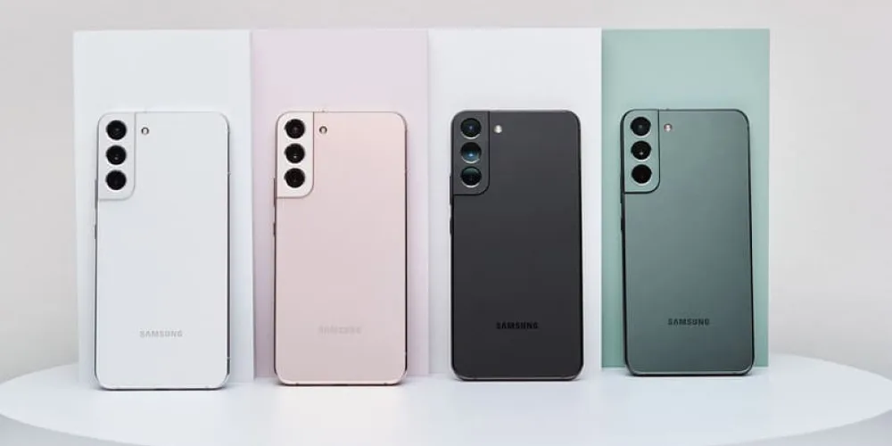 Четыре смартфона Samsung Galaxy S22 в разных цветах (белый, розовый, чёрный и зелёный), расположенные вертикально рядом друг с другом.