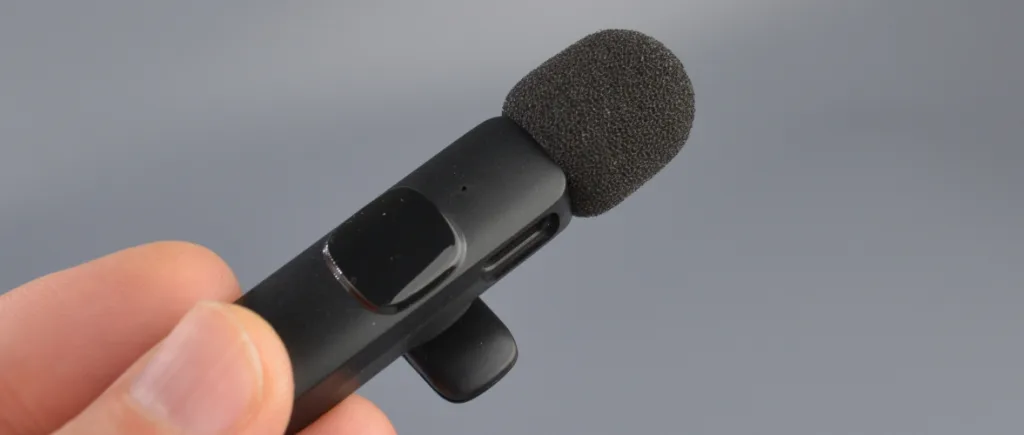 Беспроводной петличный микрофон Smile K1 с двумя микрофонами 9 Рука держит один черный беспроводной микрофон-передатчик с ветрозащитой крупным планом.