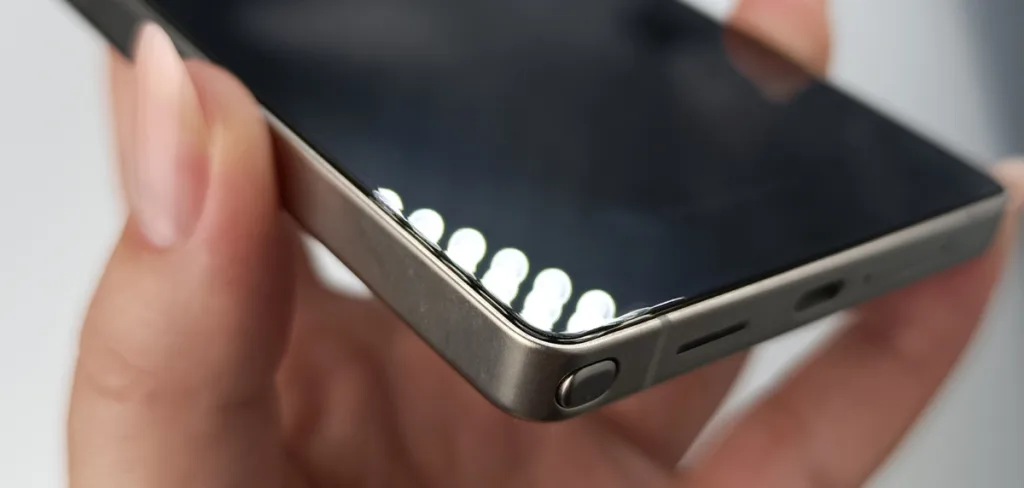 Купить гидрогелевую пленку в ТРЦ Green City 8 Крупный план угла современного смартфона, который держат в руке. Видны закругленные края дисплея и металлическая рамка.