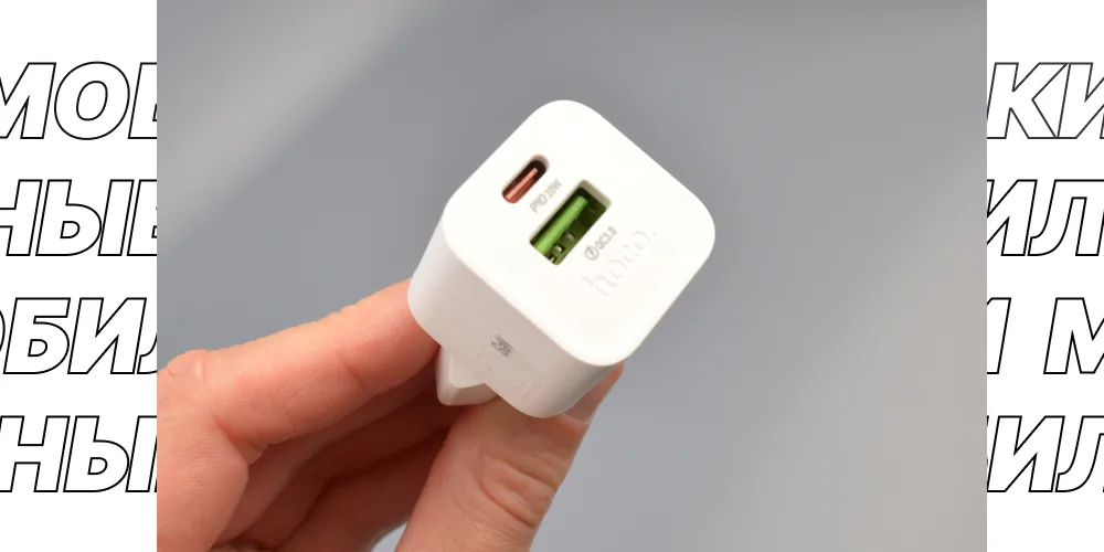 Крупный план белого зарядного устройства Hoco N65 в руке, видны порты USB-C (PD 20W) и USB-A (QC 3.0) и логотип hoco